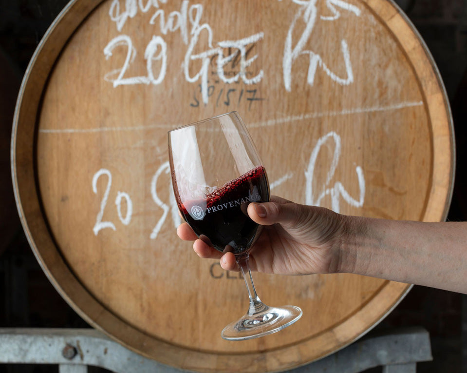 A glass of red wine in front of a wine barrel.