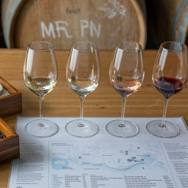 A wine flight of four glasses from white wine to red wine, on a tasting mat with map.